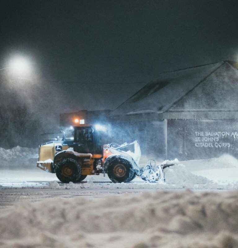 Snowplow removes snow from urban street under city lights during a cold winter night.